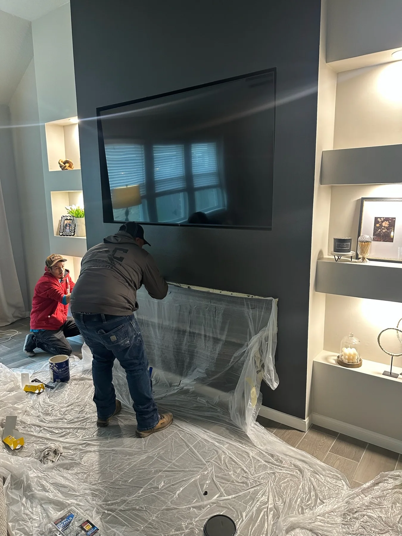 TAC crew completing detail work around a television and fireplace feature wall
